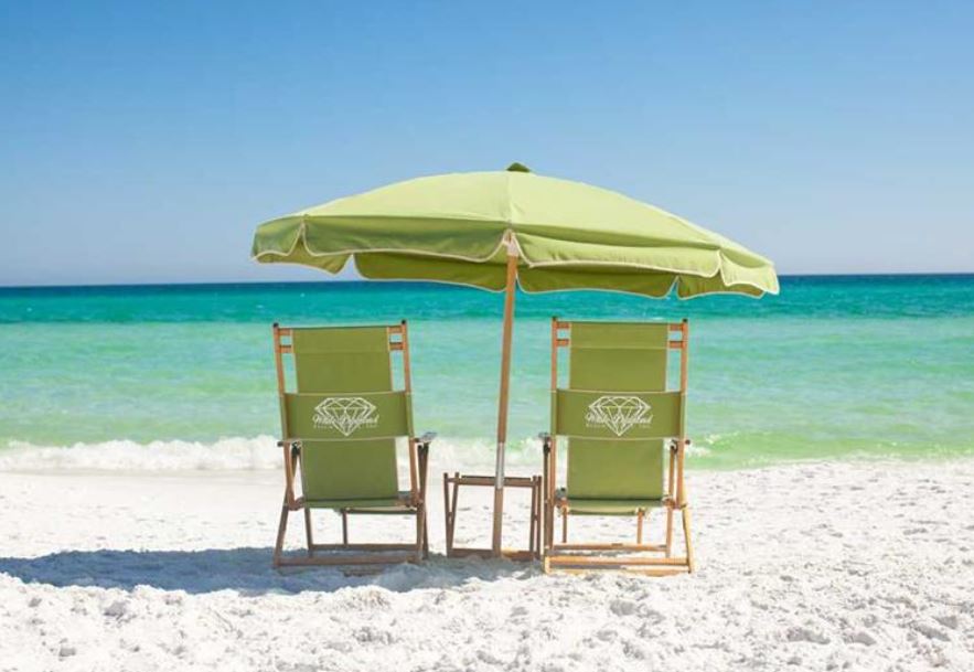 green beach chairs along with a green umbrella set up on the white sandy beach looking over the gulf of mexico